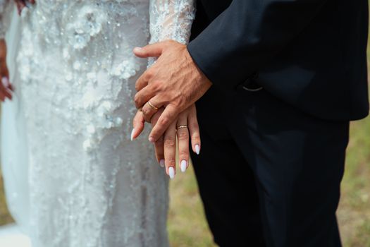 Close-up of newlyweds holding hands, showcasing elegant wedding rings and attire.