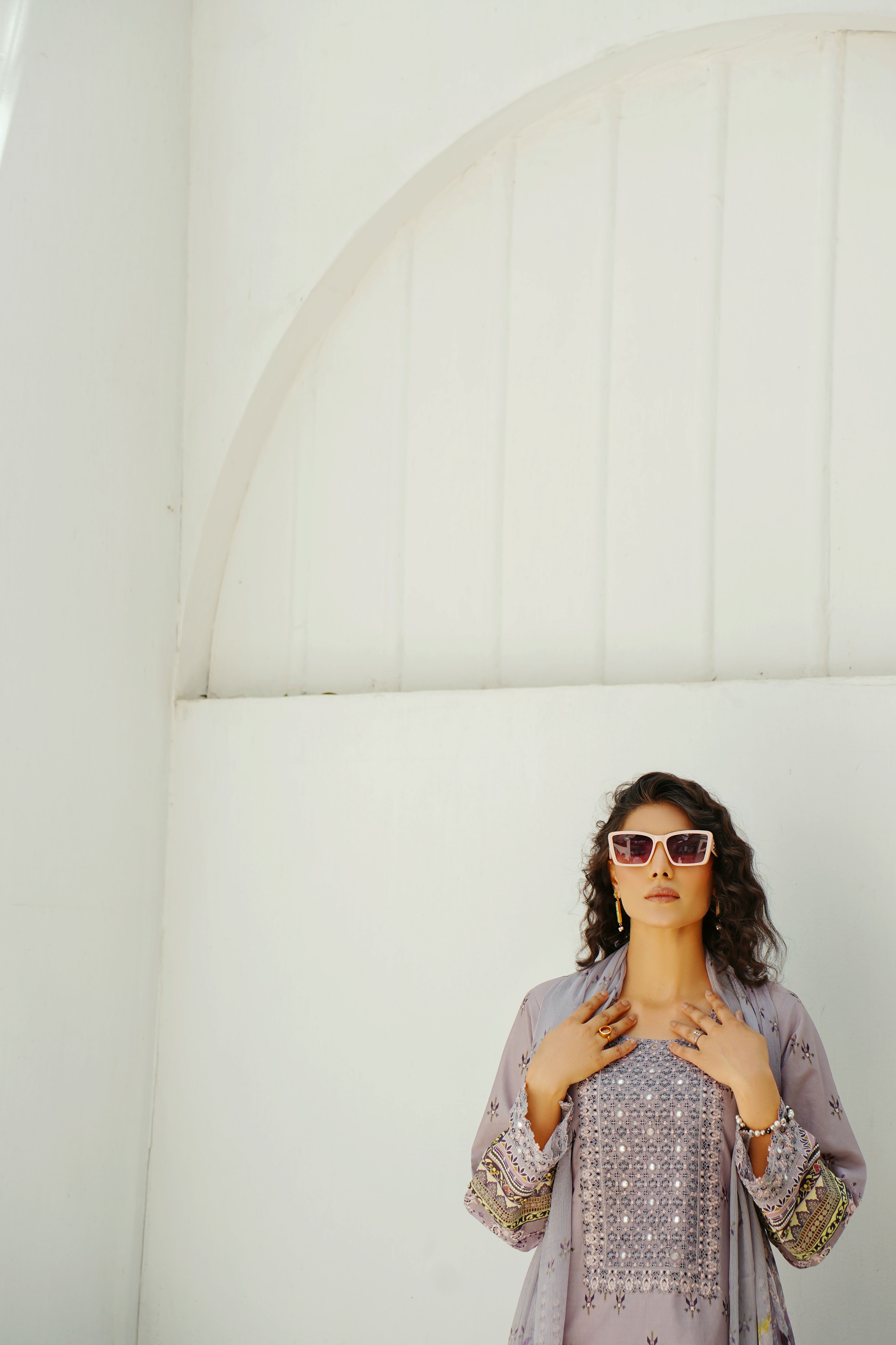 Chic woman in traditional clothing with sunglasses against white wall in Lahore, Pakistan.