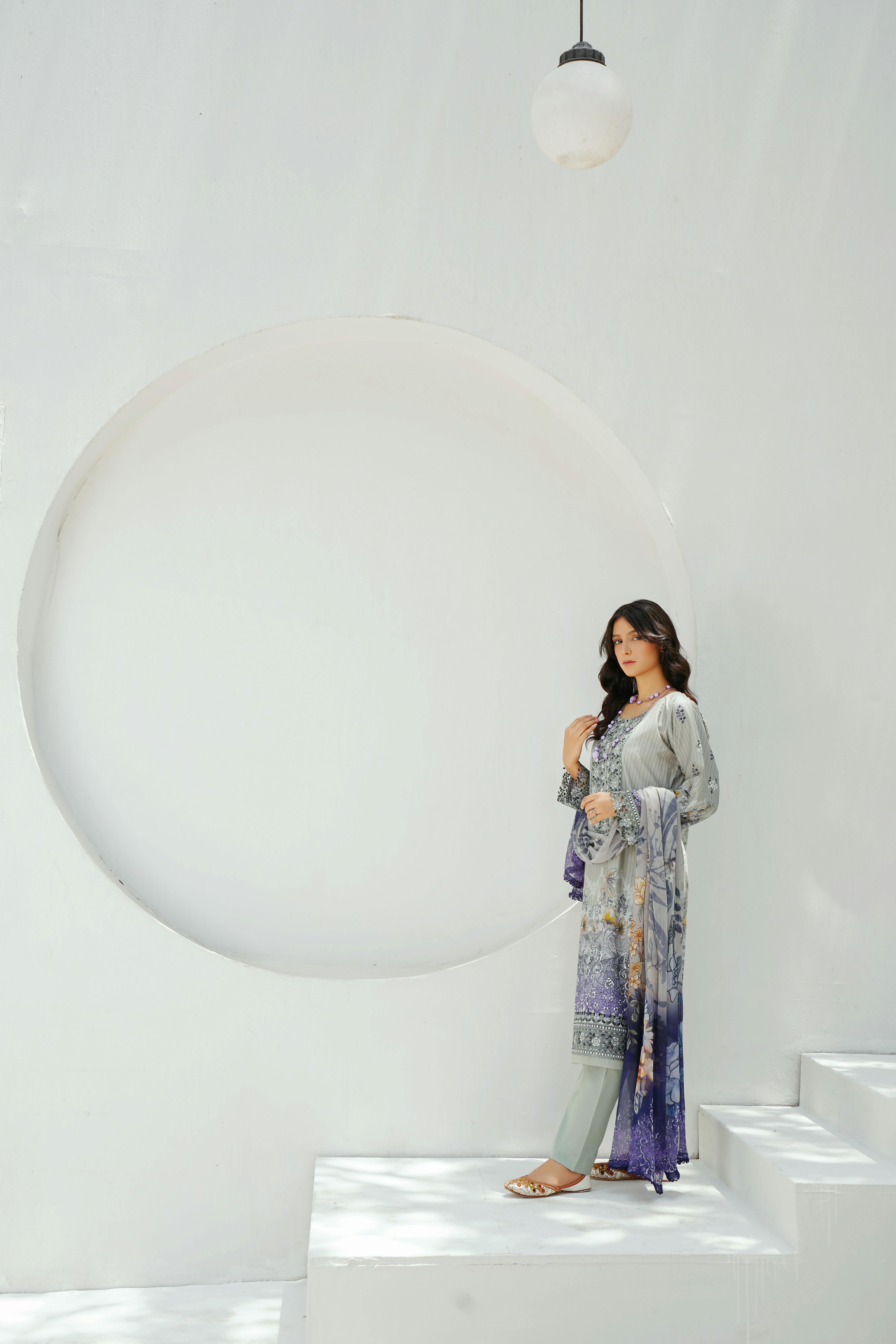 A young woman in traditional attire stands in a minimalist interior in Lahore, Pakistan.