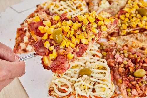 A person holding a fork over a pizza with corn and olives