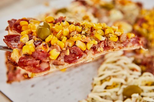 A slice of pizza with corn, tomatoes and olives