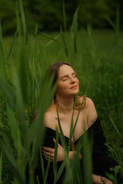 Free A woman in a black dress enjoys a quiet moment in a lush green meadow during springtime. Stock Photo