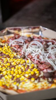 Close-up of a pizza with corn, onions, olives, and meat toppings in a box.