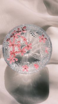 Top view of pink flowers floating in a glass bowl on white fabric bathed in sunlight.