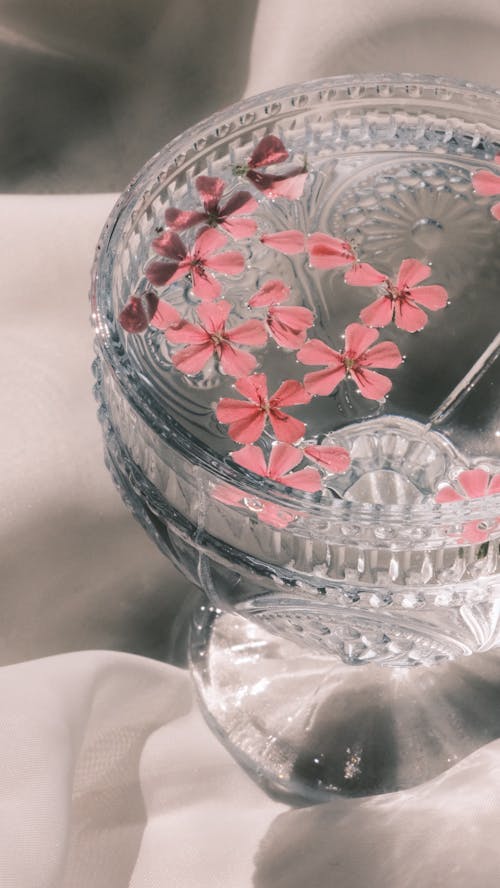 A glass with pink flowers in it on a bed