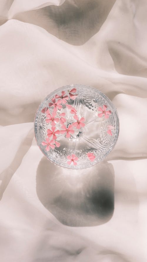 A glass with pink flowers on it sitting on a white cloth