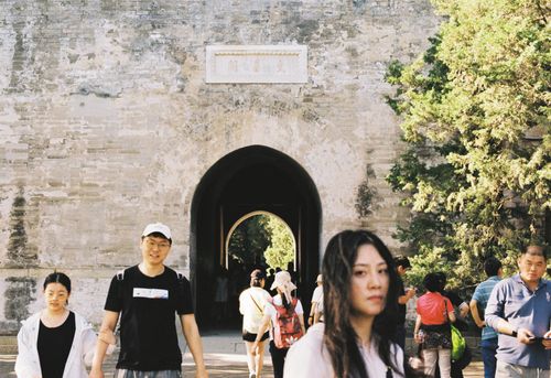 Free An urban scene with diverse pedestrians walking near a historic stone archway, illuminated by daylight. Stock Photo