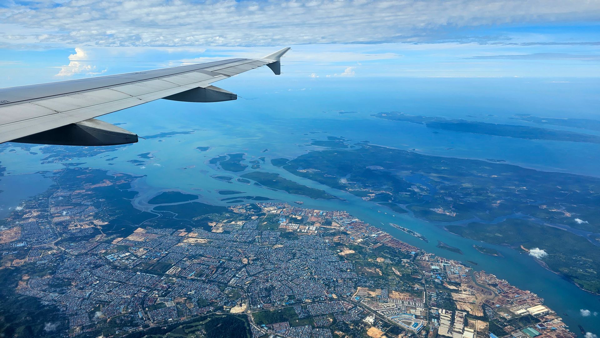 Aerial view from airplane showcasing a cityscape and coastline beneath a wing on a clear day.