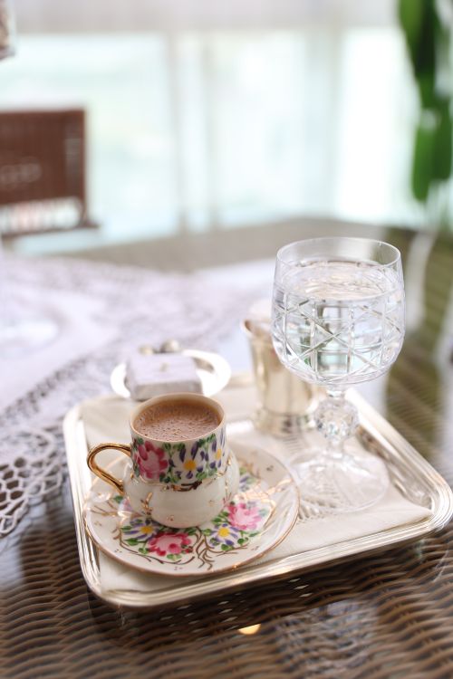 Free A beautifully arranged coffee cup and glass of water on a floral tray with soft ambient lighting. Stock Photo
