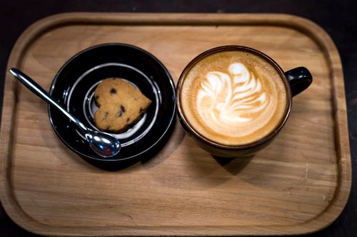 Free Close-up of a cup of latte with latte art and a cookie on a wooden tray. Stock Photo