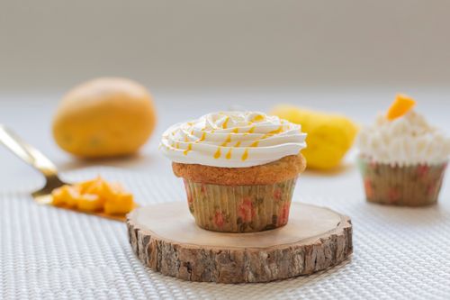 Free Close-up of a mango cupcake with cream frosting, surrounded by fresh mango pieces. Stock Photo