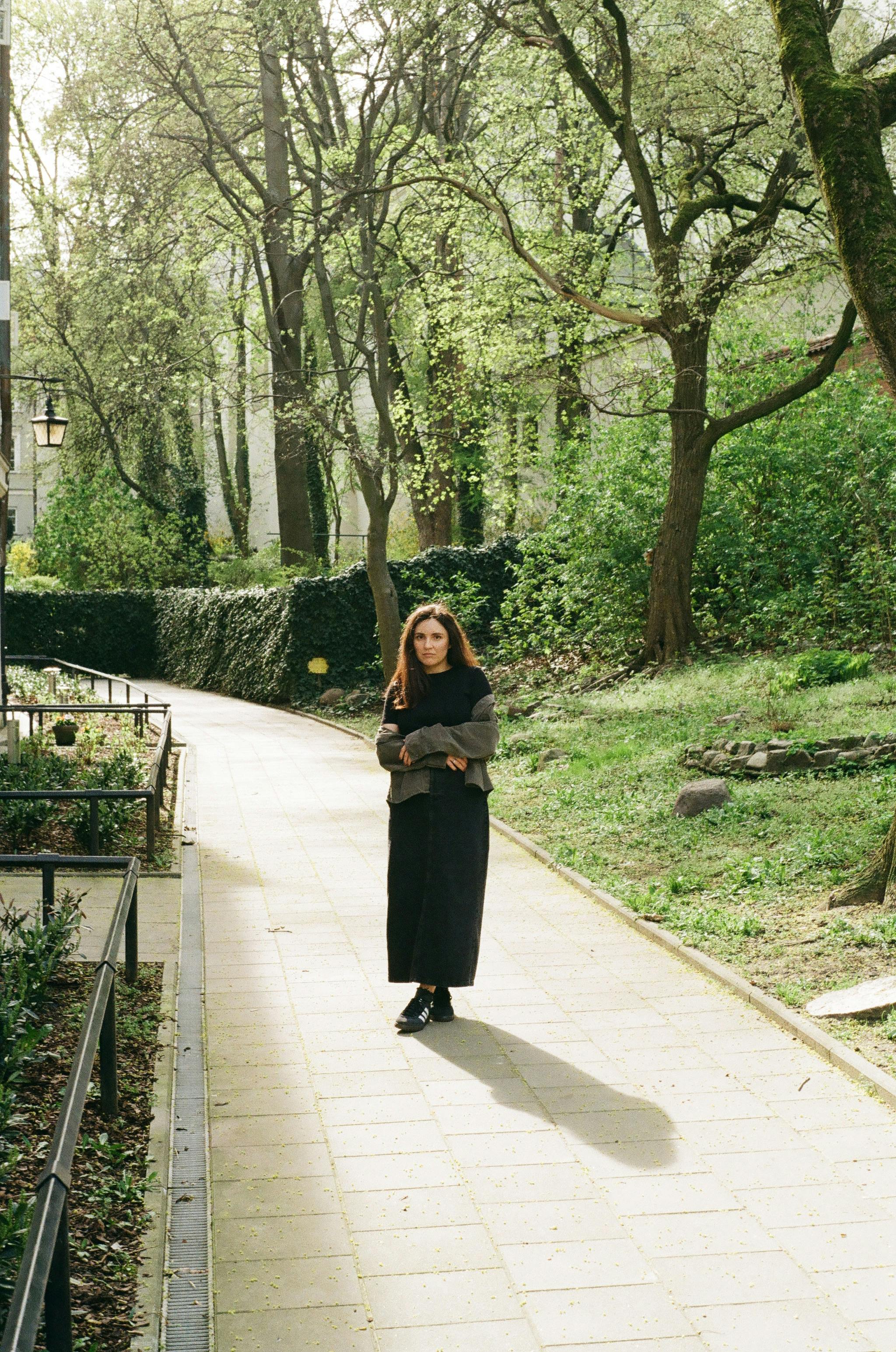 Young woman in a black dress walking in a sunlit park during springtime.