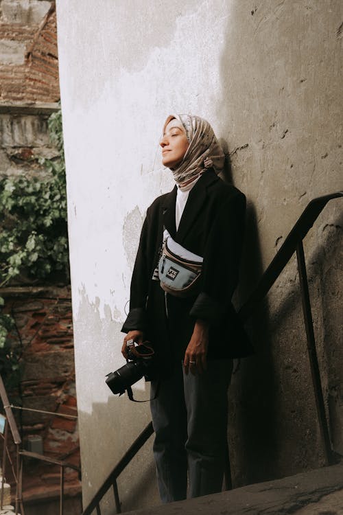 A woman in a hijab leaning against a wall