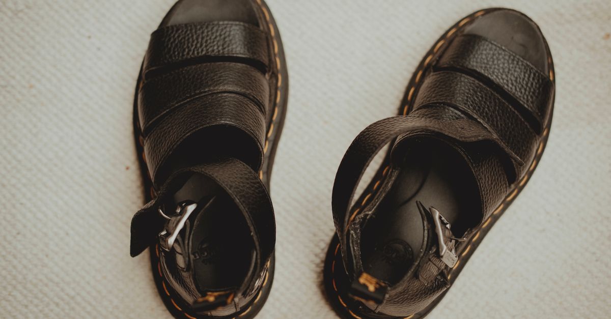 Close-up of black leather sandals with buckle straps on a textured beige surface.