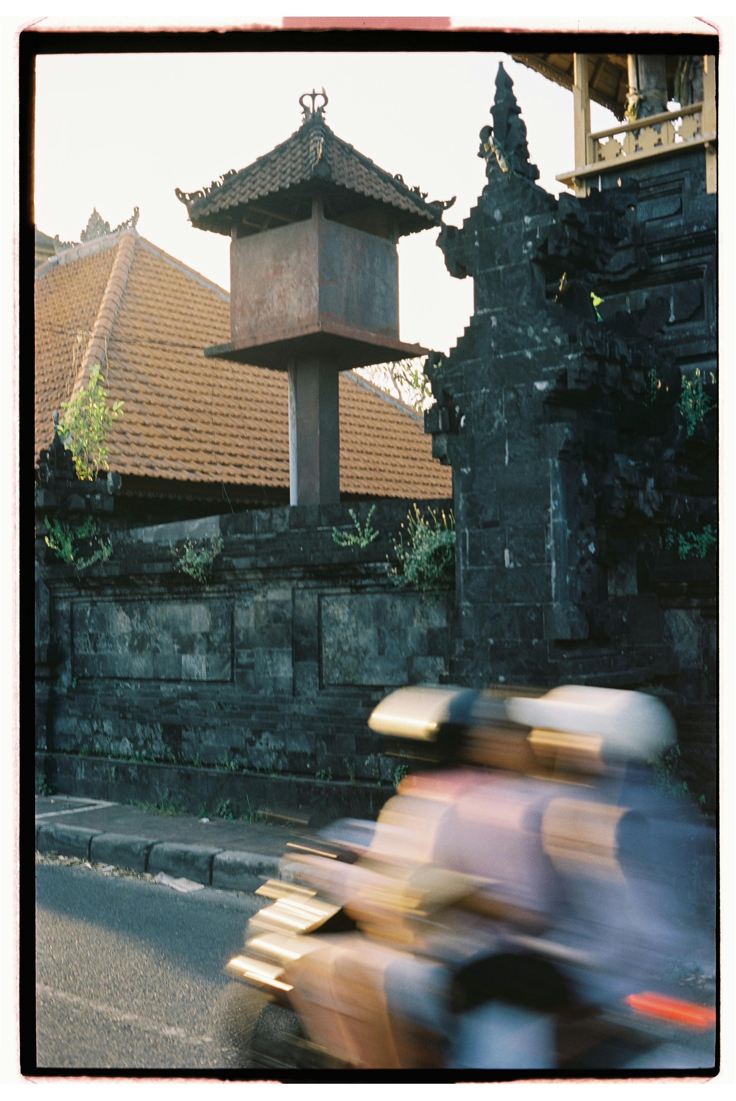 Motorbike passing historical architecture in Bali, Indonesia, showcasing dynamic motion and cultural detail.