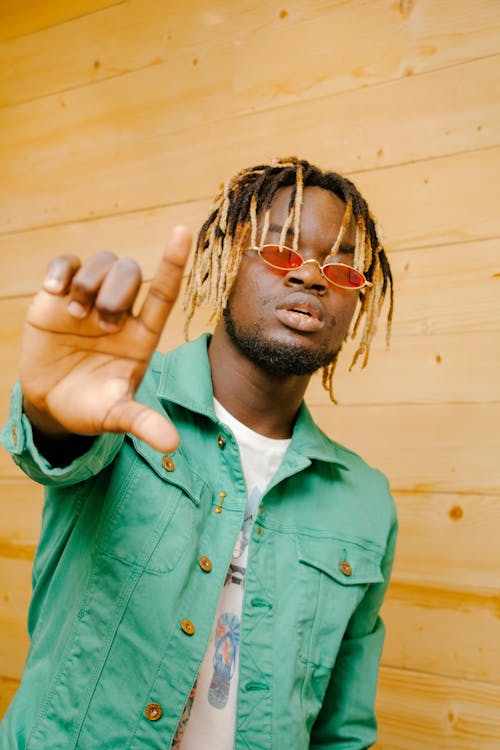 Photo of Man Posing With Hand Out Doing Hand Gesture Standing In Front of Wooden Wall