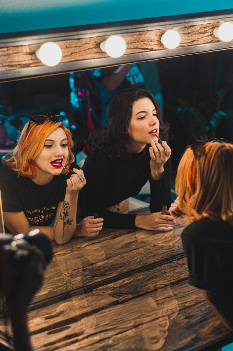 Two Women Applying Lipsticks In Front Of Vanity Mirror