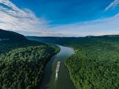 航拍照片显示，一艘驳船在清澈的蓝天下，沿着蜿蜒的河流穿过郁郁葱葱的森林