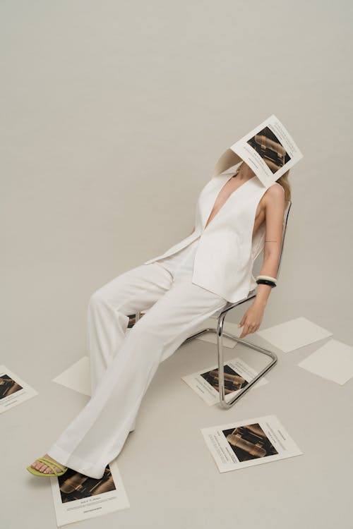 A woman in white sitting on a chair with a paper on her head