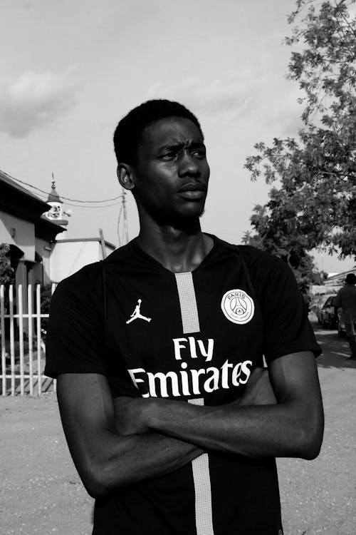 Grayscale Photo of Man in PSG Jersey With His Arms Crossed Looking Away