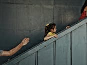 一名穿着黄色上衣的孩子，在两名成年人的帮助下，正在爬户外的混凝土楼梯