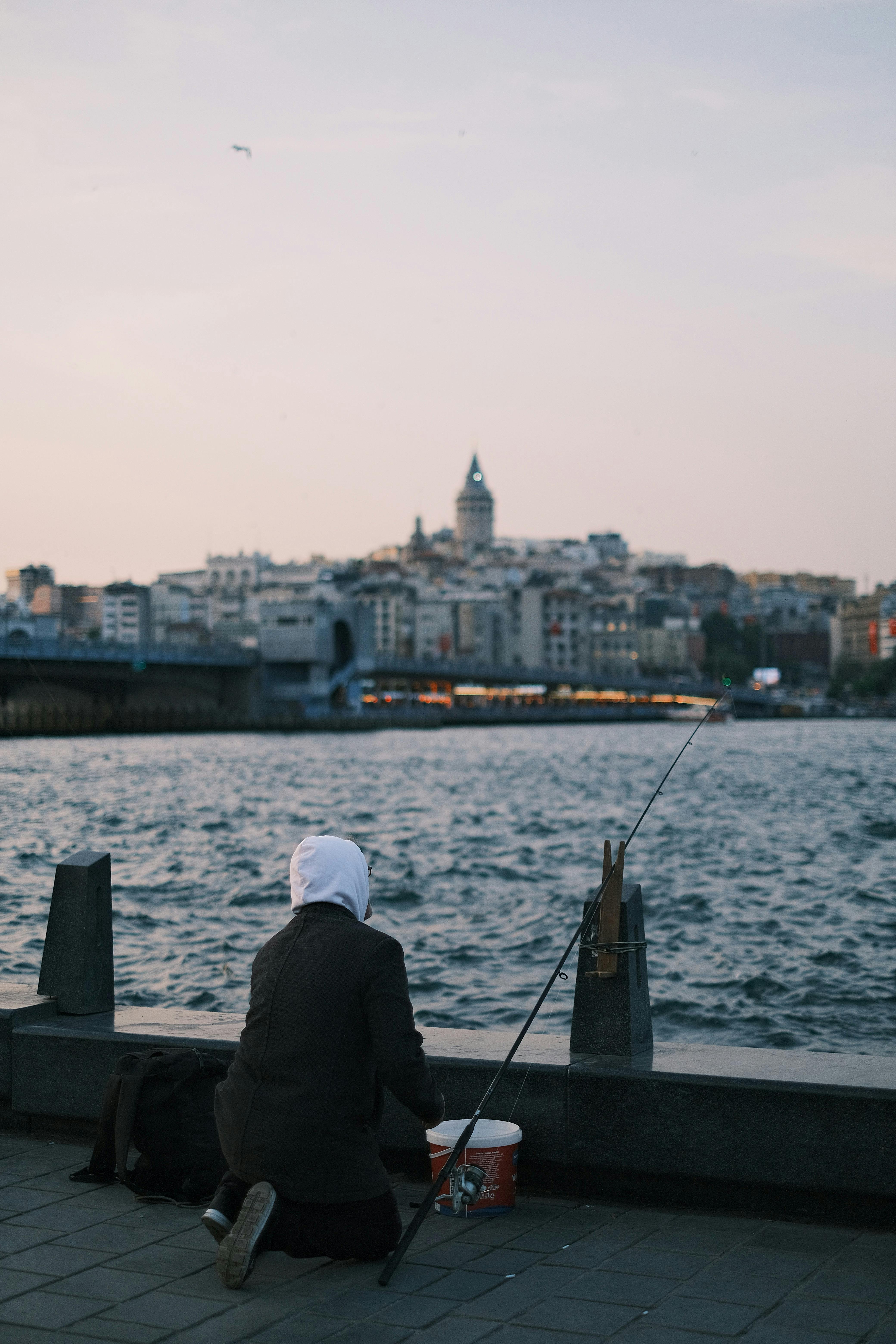 A person fishing by the sea in Istanbul with the iconic Galata Tower in the background during the day.