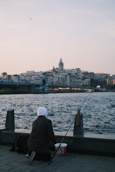 A person fishing by the sea in Istanbul with the iconic Galata Tower in the background during the day.