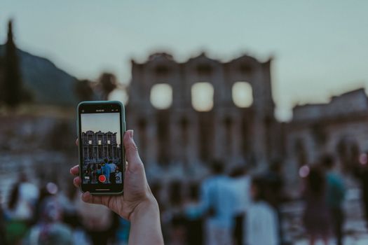 A blurred image of tourists photographing ancient ruins with a smartphone at dusk.