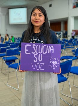 A young woman holds a sign saying 'Escucha Su Voz' in a venue in Ciudad de México, Mexico.