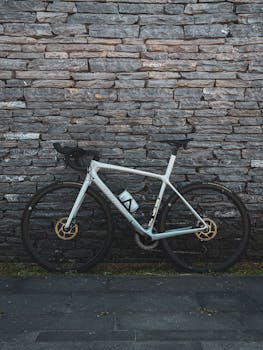 Modern bicycle leaning against a textured stone wall in a city setting.