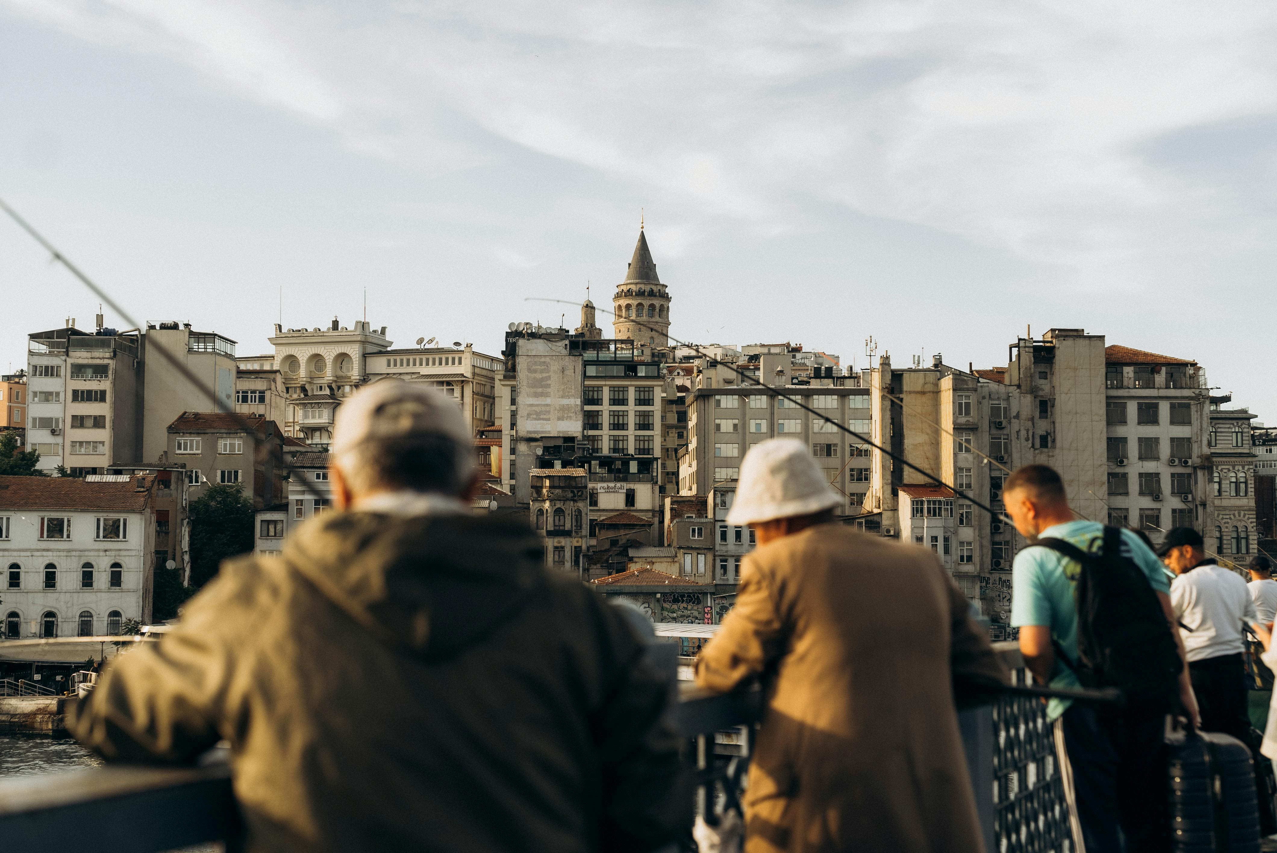 Men fishing on Galata Bridge with Galata Tower and Istanbul skyline in the background.