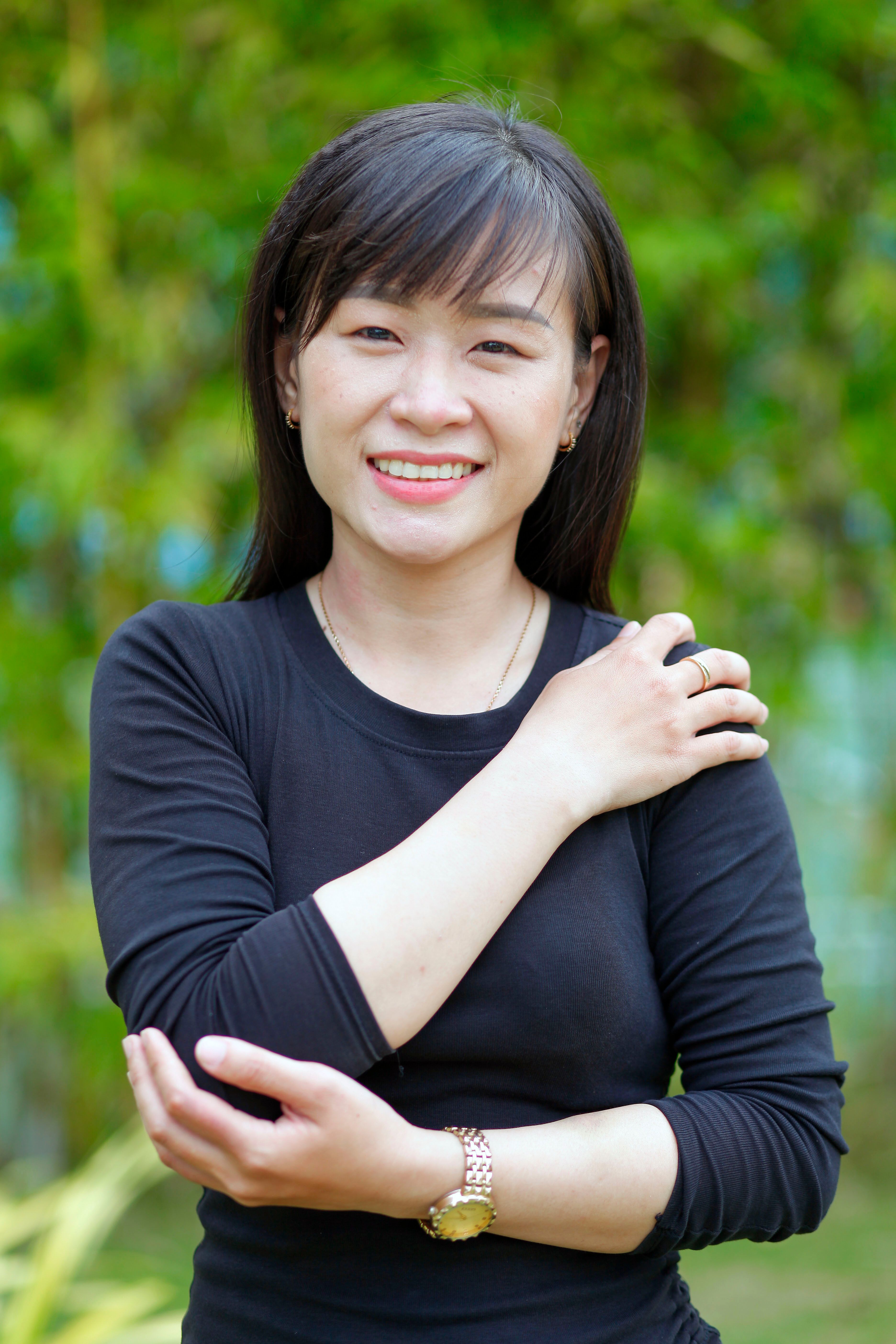 A cheerful woman in a black blouse, posing outdoors with a vibrant green background.