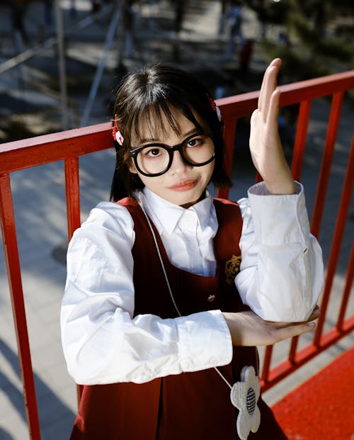 A girl in glasses and a red dress is waving