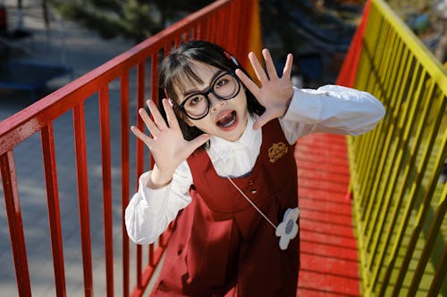 A girl in glasses and a red dress is making a funny face