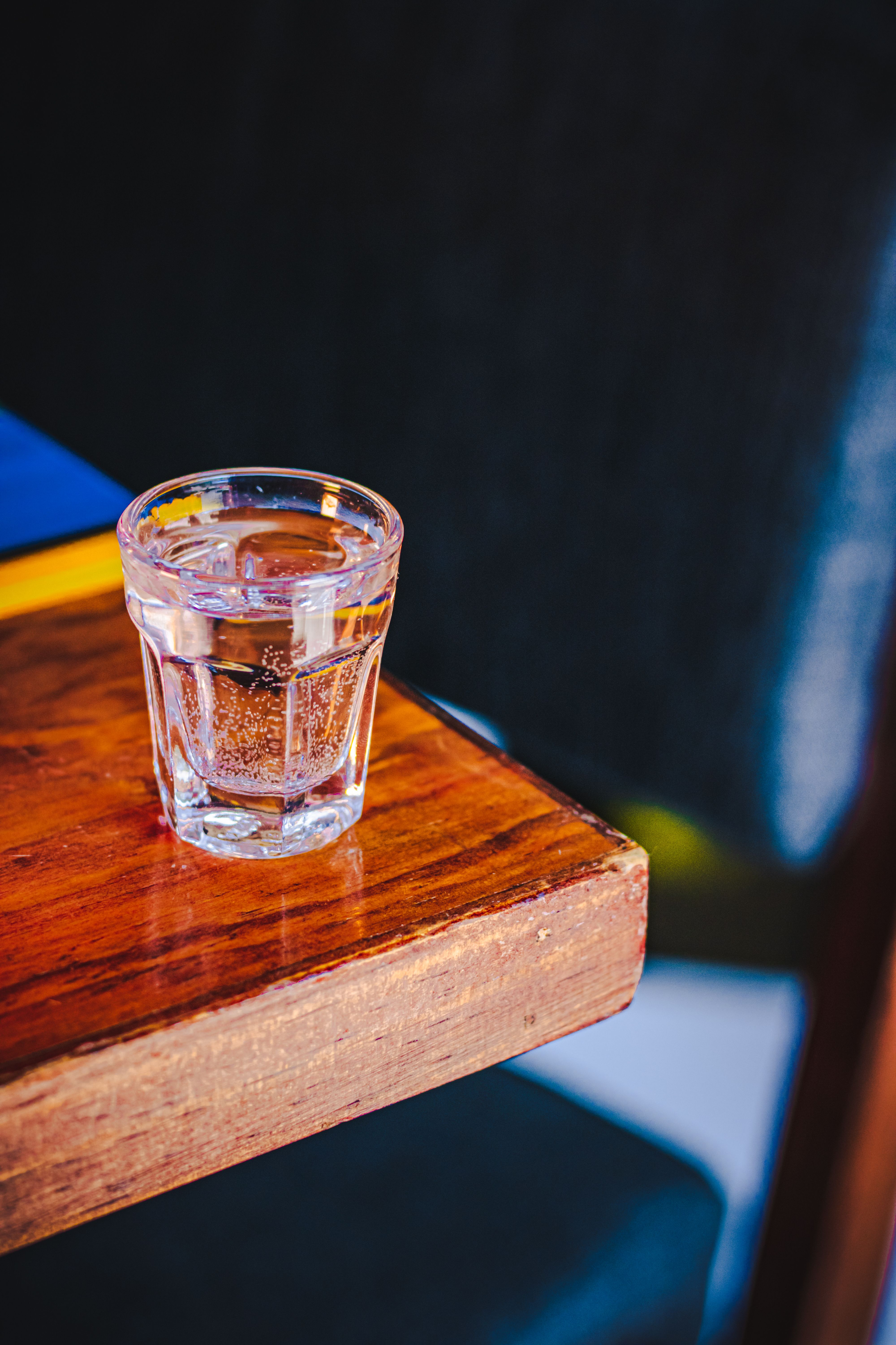 A tequila shot glass on a wooden table with a colorful background in a bar setting.