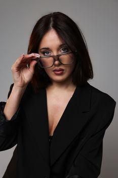Elegant studio portrait of a woman in a black jacket with eyeglasses, posing confidently.
