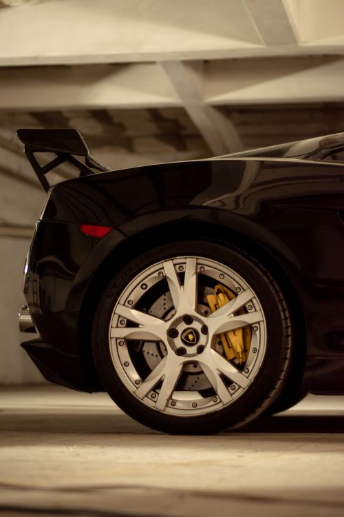 Free Close-up of a black luxury car wheel with yellow brake calipers parked indoors. Stock Photo
