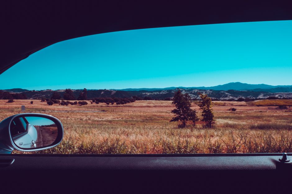View of a vast field and mountains from inside a car, showcasing a beautiful summer day.