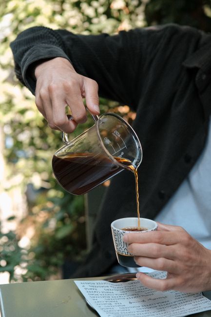 Close-up of a man pouring coffee into a cup at an outdoor cafe setting.