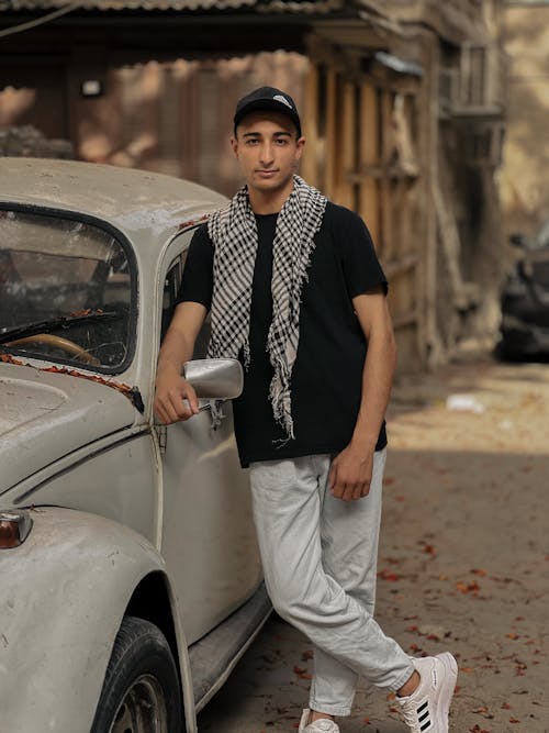 A young man standing next to an old car