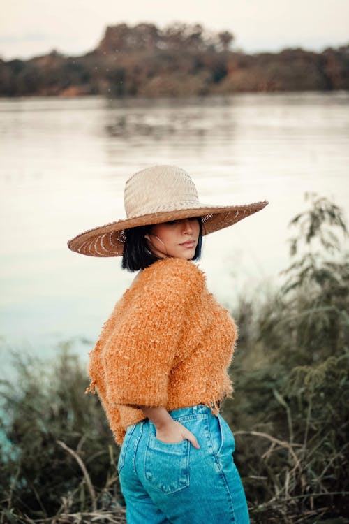 免費 太陽帽，橙色針織上衣和藍色牛仔下裝的女人的照片 圖庫相片