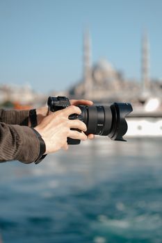 Close-up of hands holding a camera, capturing the Bosphorus with Istanbul's iconic skyline in the background.
