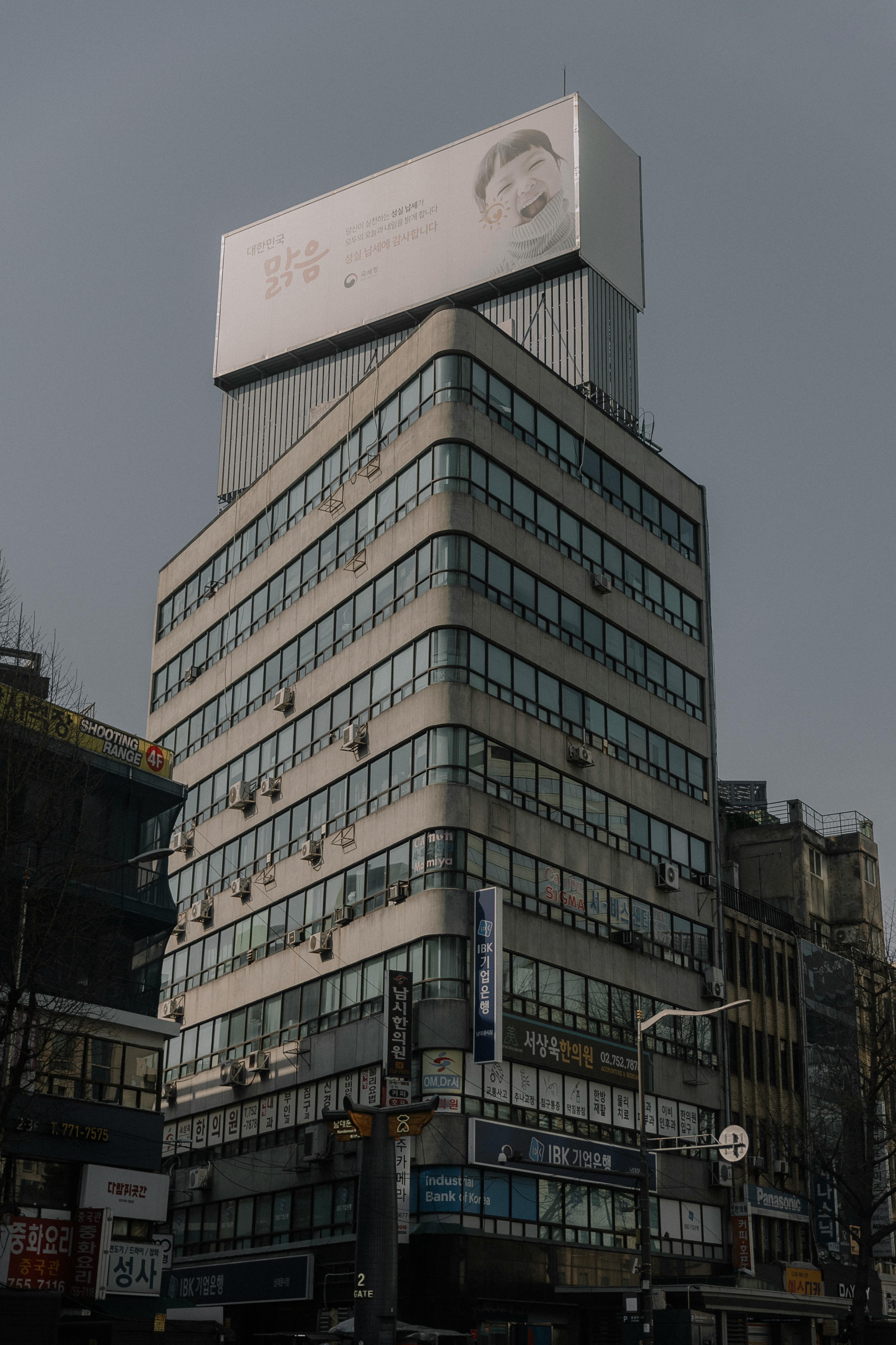 Free A tall office building with a prominent billboard, capturing urban architecture in daylight. Stock Photo