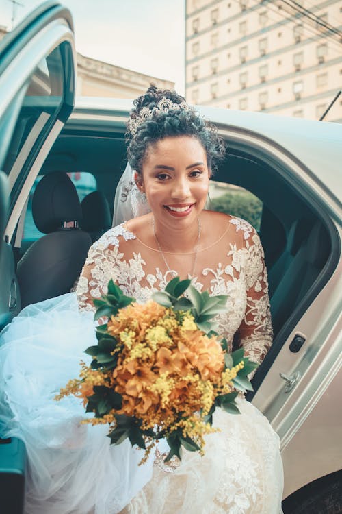 Bride in wedding dress sitting in car with bouquet