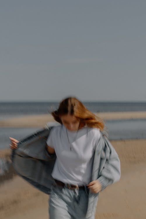 A woman walking on the beach with a white shirt