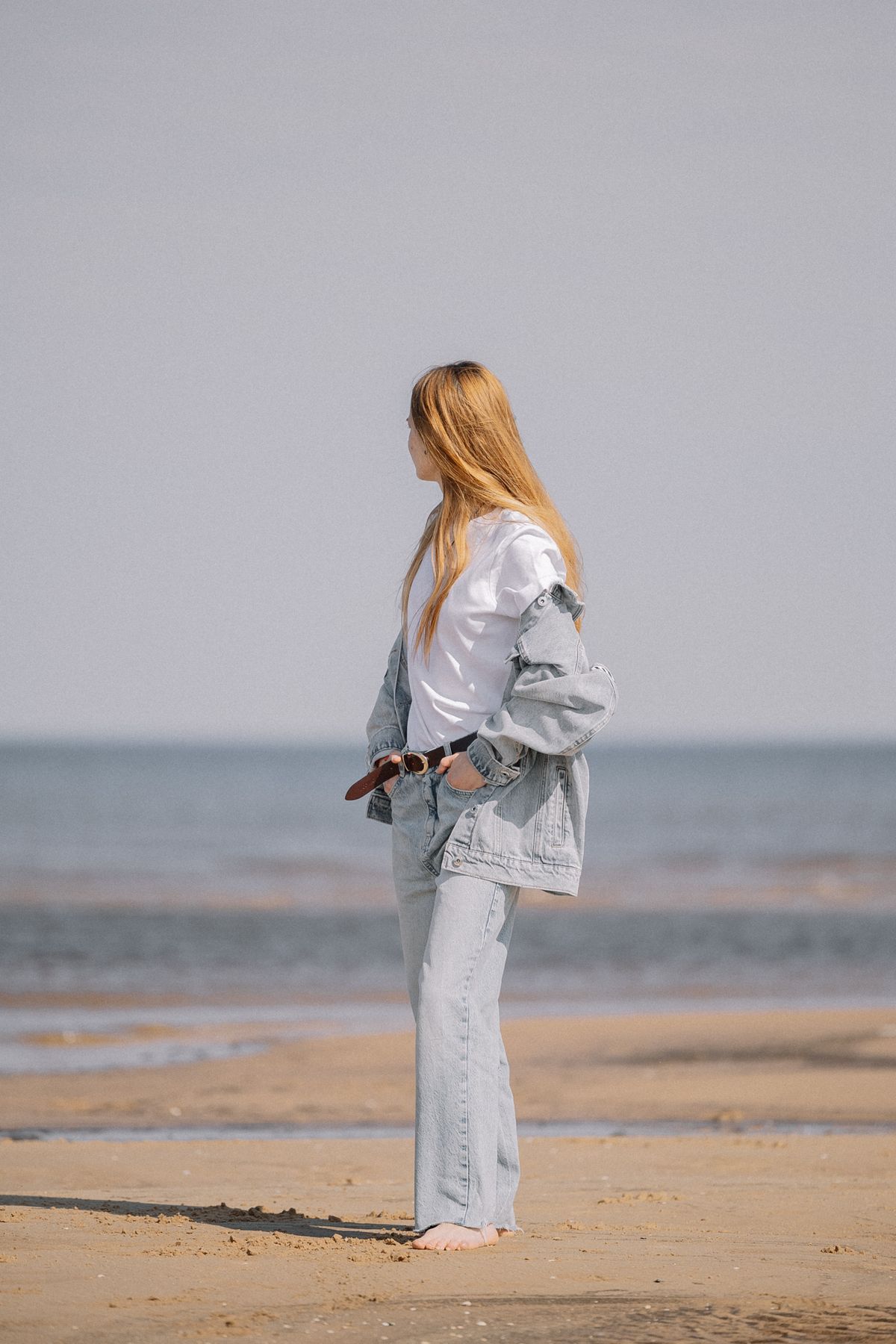 A blonde woman in jeans and a jean jacket on a beach — double denim done well