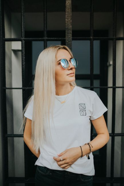 Fashionable blonde woman wearing casual clothing and sunglasses, standing against a backdrop with long hair flowing.