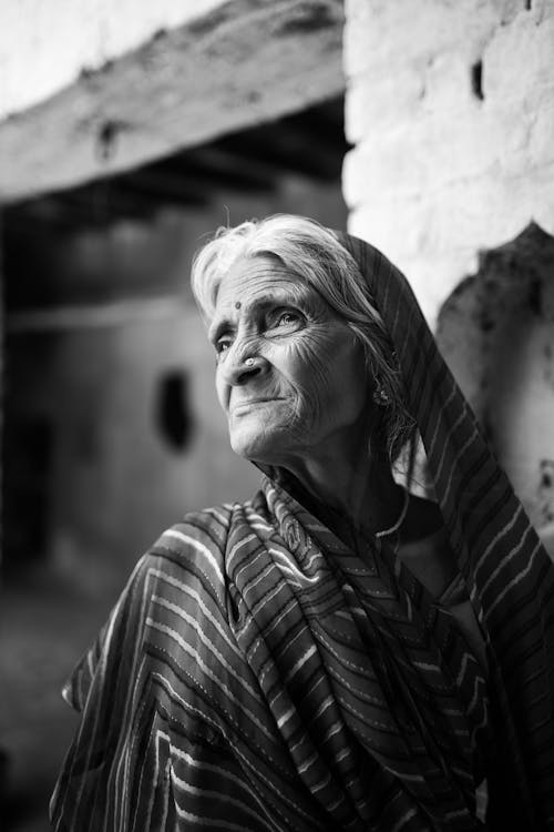 An old woman in a sari standing in front of a wall