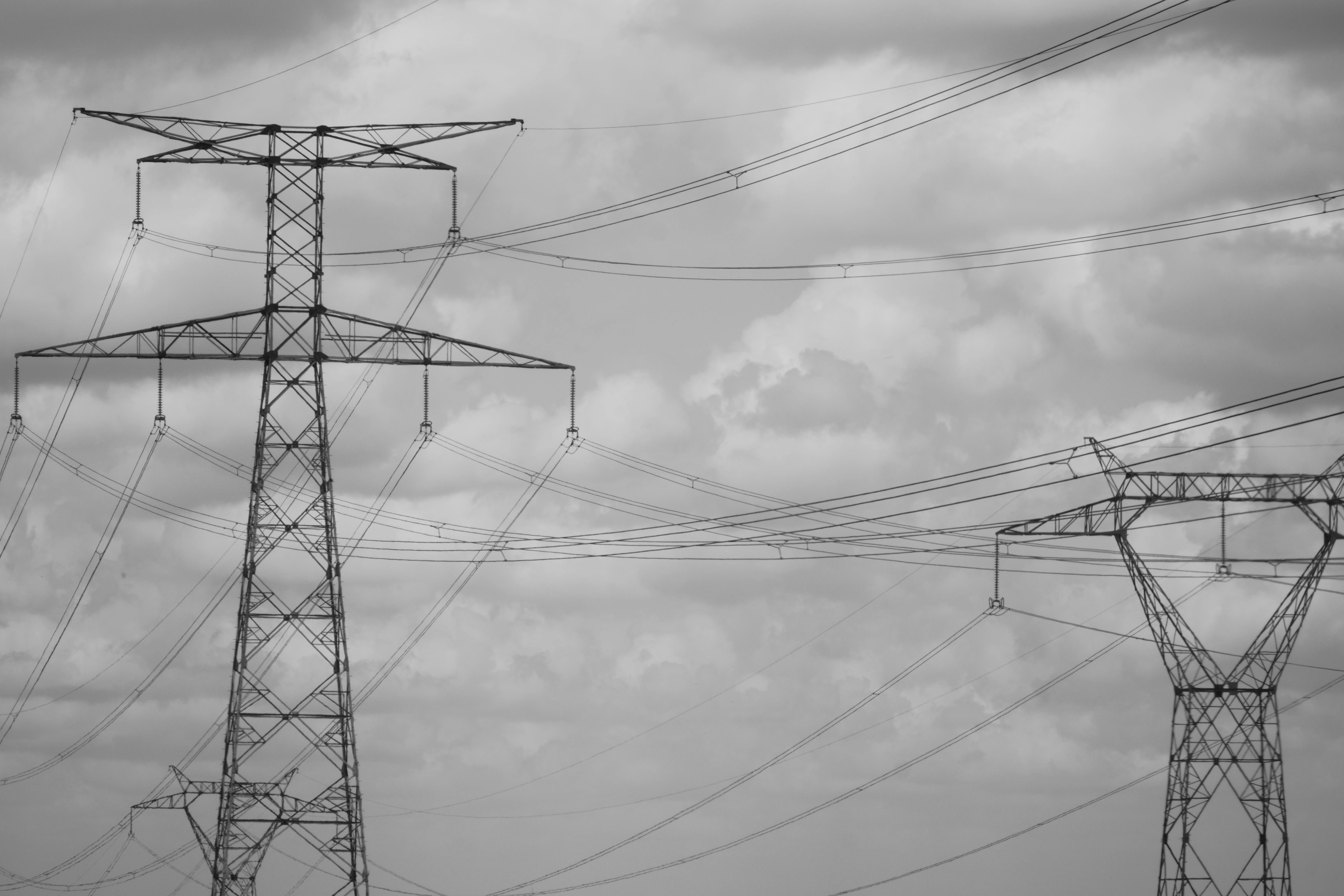 Dramatic black and white photo of high voltage power lines in the sky, showcasing industrial steel structures.