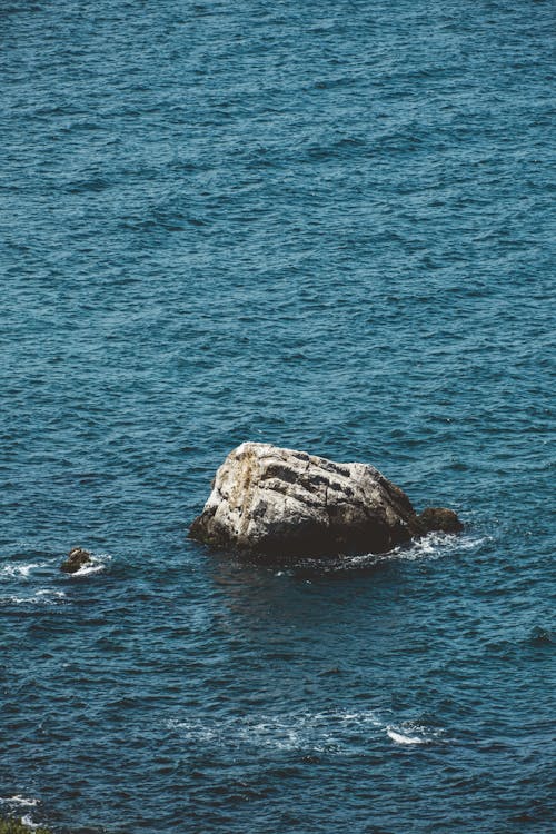 A rock in the ocean with a bird flying over it
